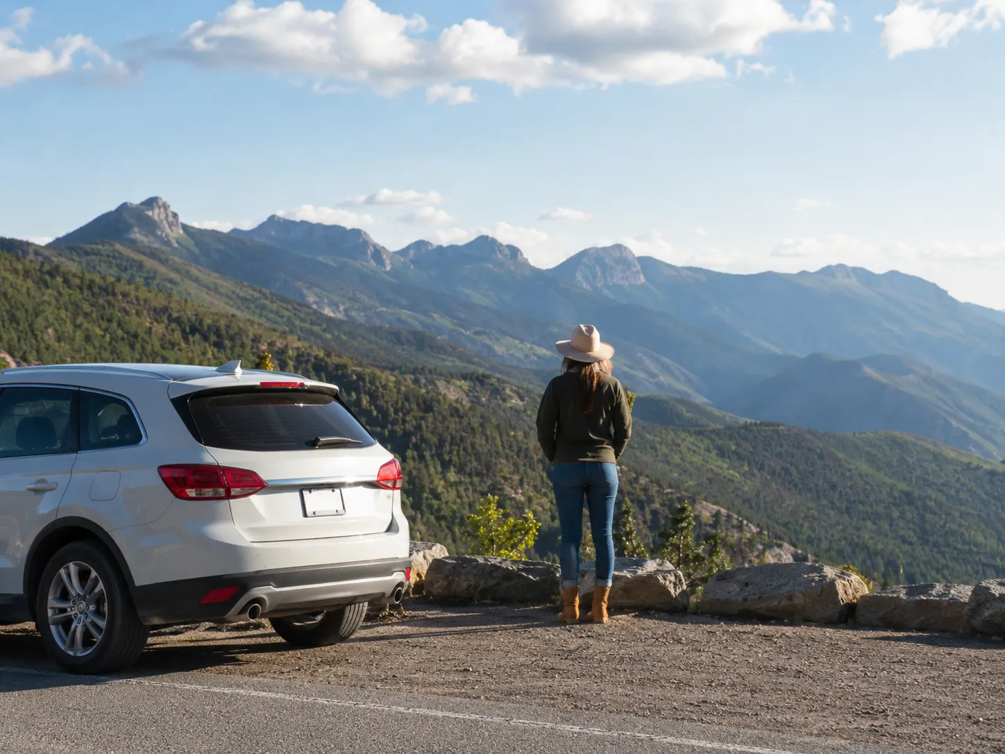 Scenic road trip viewpoint with car parked near mountains and traveler looking away.