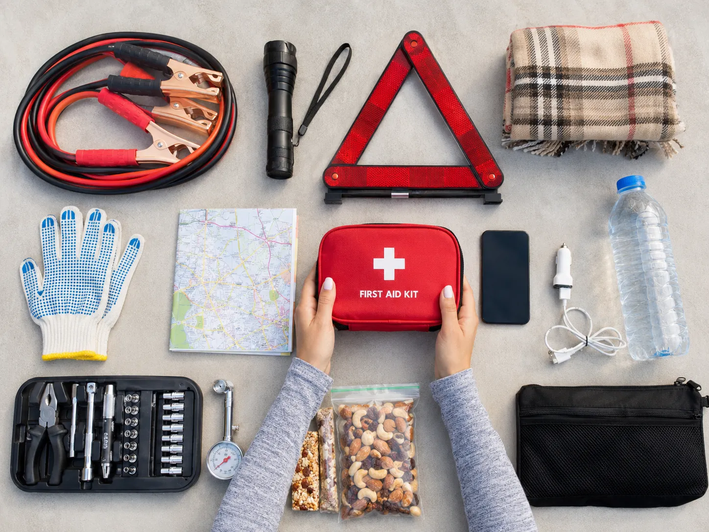 Complete road trip emergency kit with first aid supplies, jumper cables, flashlight, and safety tools.
