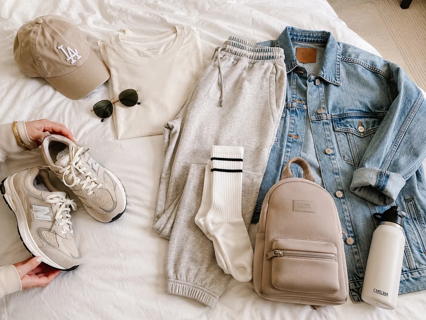 Comfortable road trip outfit flat lay with sneakers, jacket, sunglasses, and backpack.